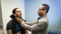 Male doctor examines adolescent's throat.
